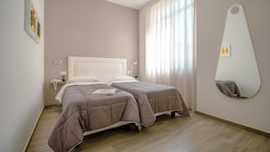 Ein Schlafzimmer mit zwei Betten, einem großen Spiegel und einem Fenster mit Vorhängen.