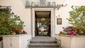 Der Eingang des Bruman Hotels mit deutlicher Beschilderung, Stufen, die zum Eingang führen, und Pflanzen in Töpfen auf beiden Seiten.
