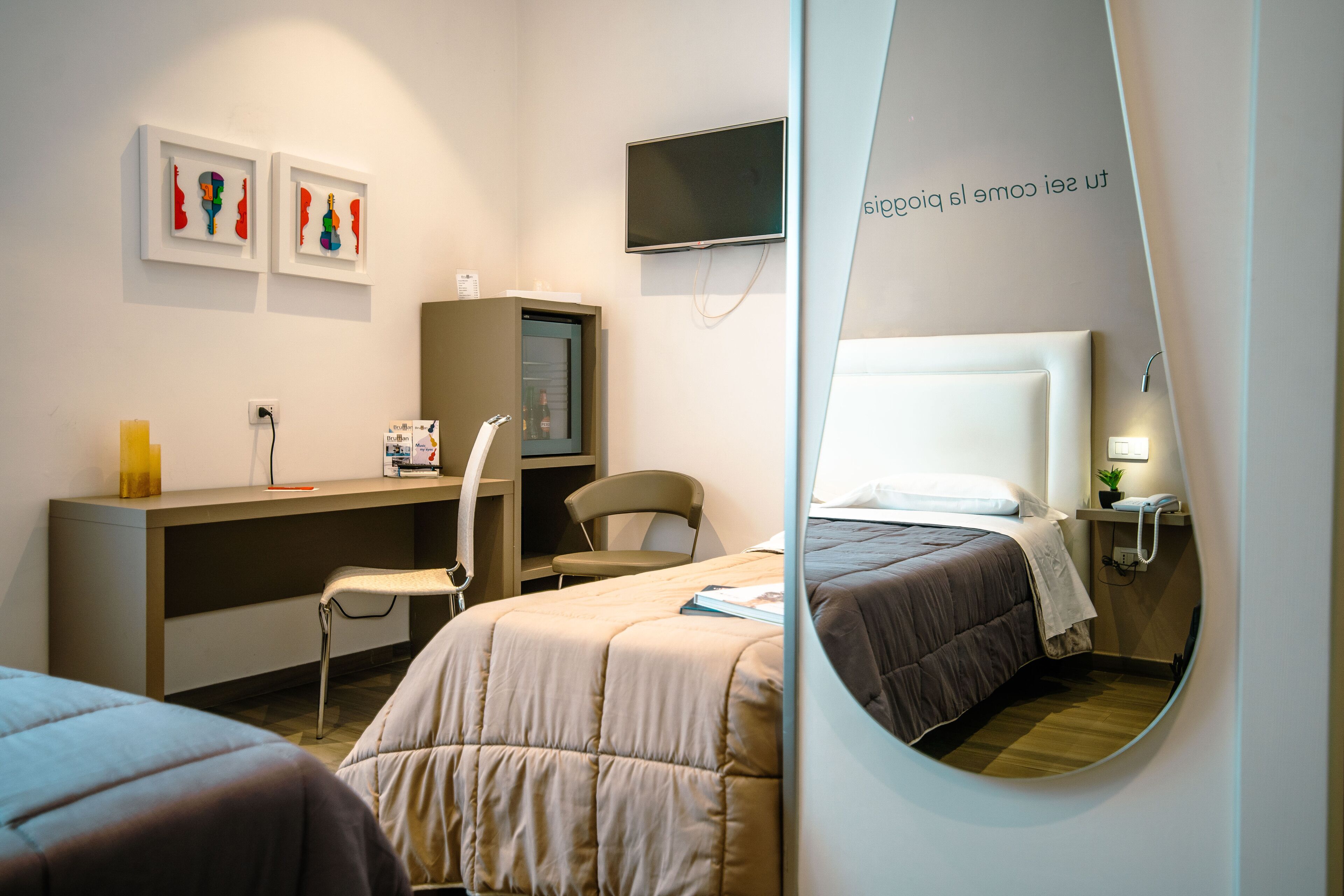 Ein Hotelzimmer mit zwei Betten, einem Schreibtisch, einem Sessel, einem Fernseher und Bildern an der Wand.