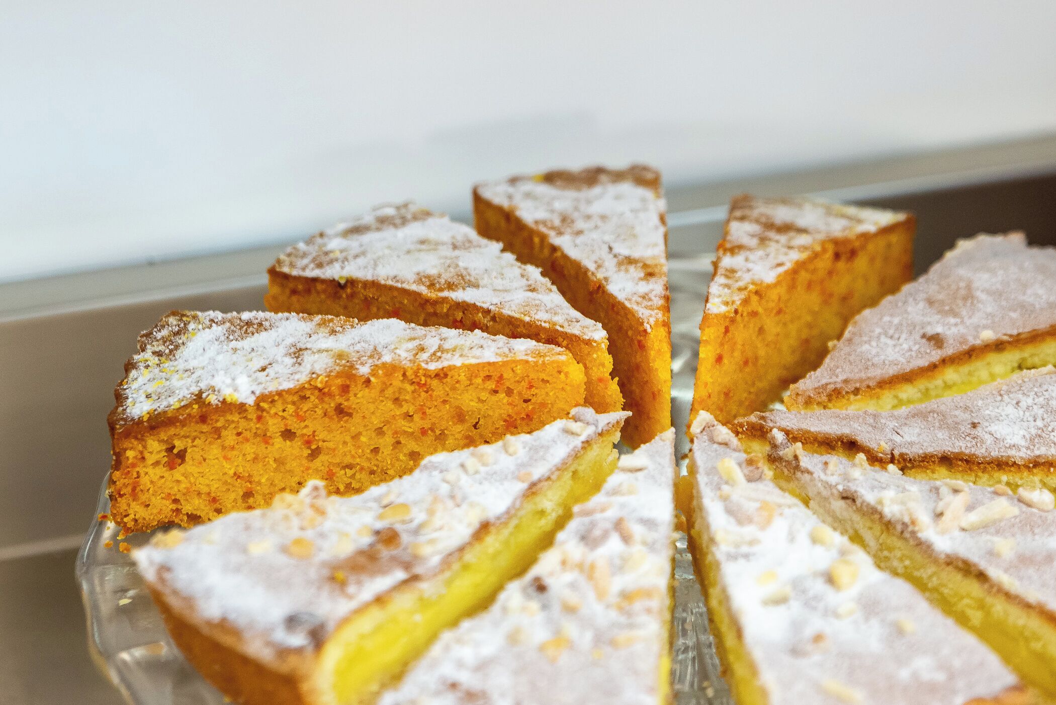 Una torta con zucchero a velo e fette su un piatto di vetro trasparente.