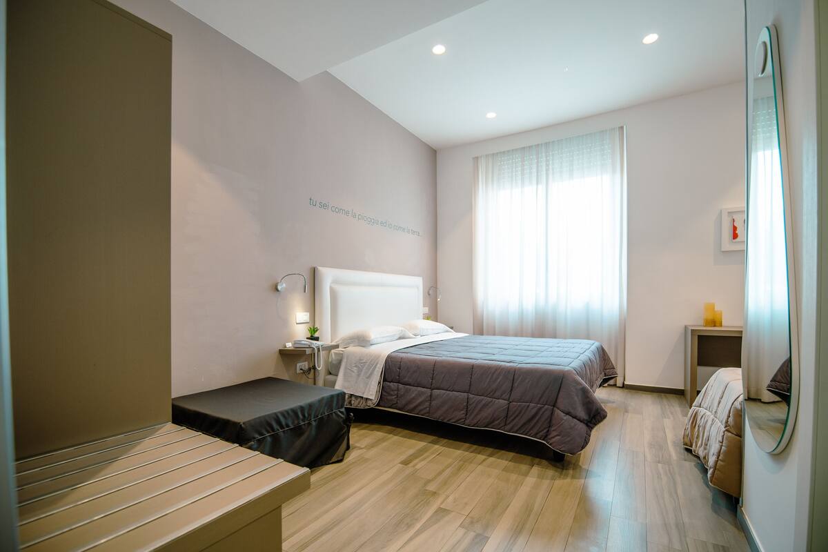 Een moderne slaapkamer met een groot bed, nachtkastjes, een bankje en een spiegel.