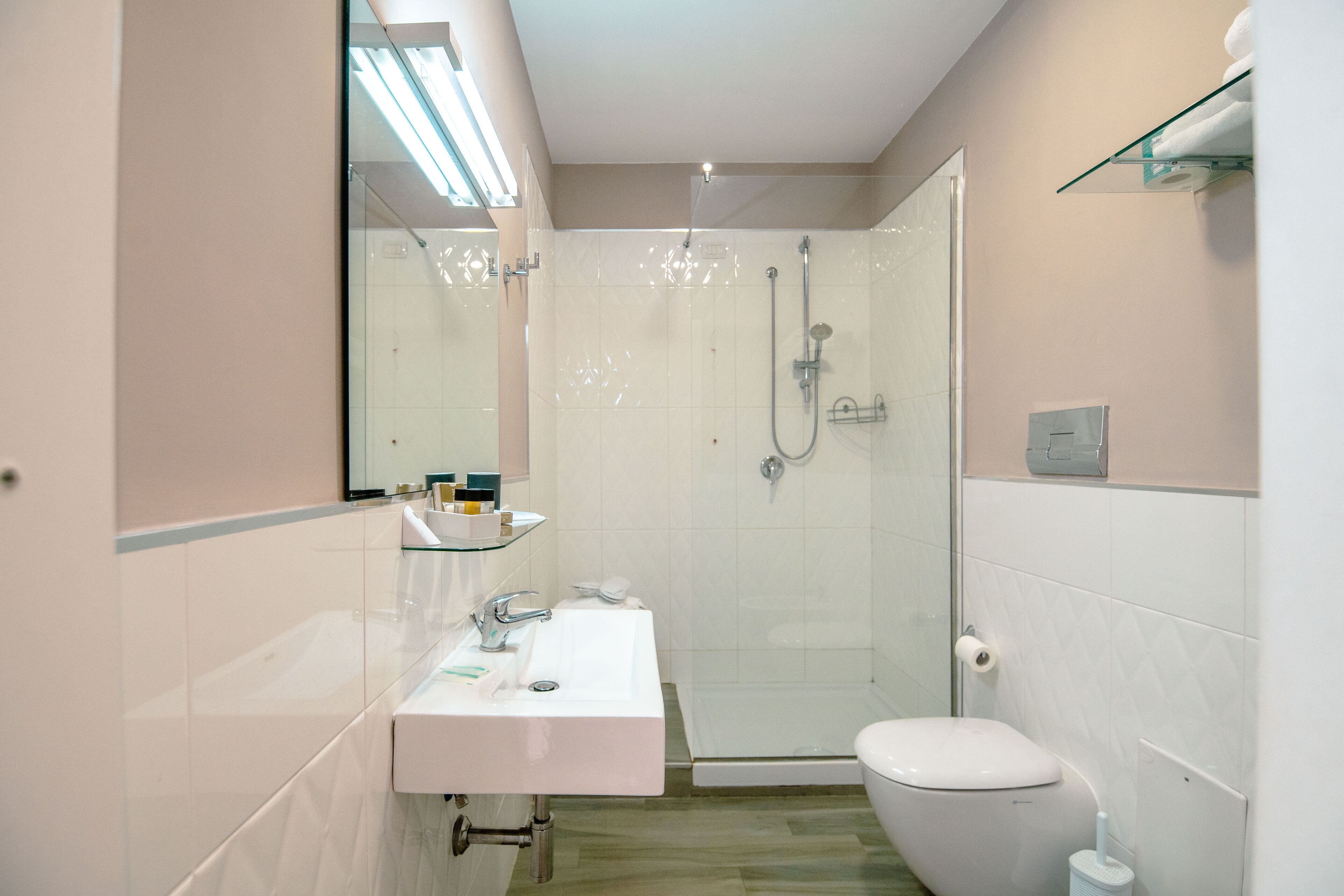 Un bagno moderno con box doccia in vetro, lavandino bianco con specchio e un water.