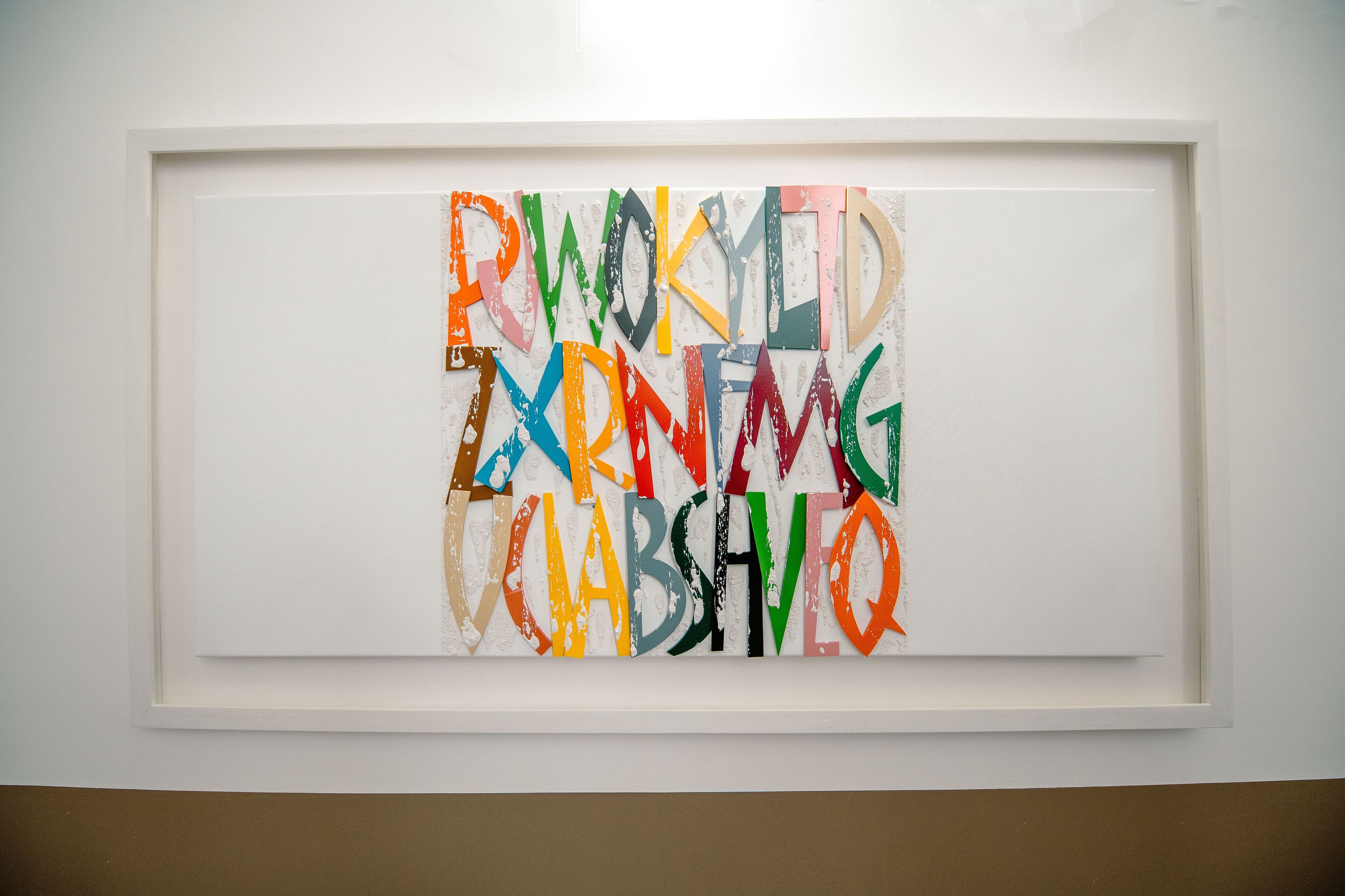 A framed artwork with colorful letters on a white wall.