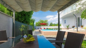 Un espace extérieur abrité comprenant une piscine, des fauteuils en osier et une table garnie de fruits.