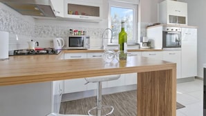 Une cuisine moderne avec des armoires blanches, un plan de travail en bois, un four à micro-ondes encastré, une cuisinière et une fenêtre laissant entrer la lumière naturelle.