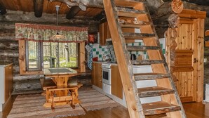 L'interno accogliente di una baita rustica, con un tavolo di legno, sedie, una cucina con un fornello e una scala in legno.