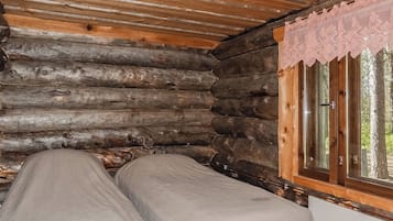 A log cabin room with a bed, a window with a lace curtain, and a wooden ceiling.