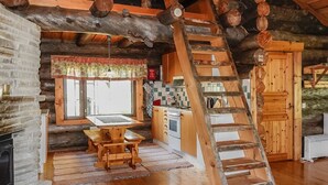 Interno di una baita rustica con un tavolo da pranzo in legno, un angolo cottura e una scala in legno.