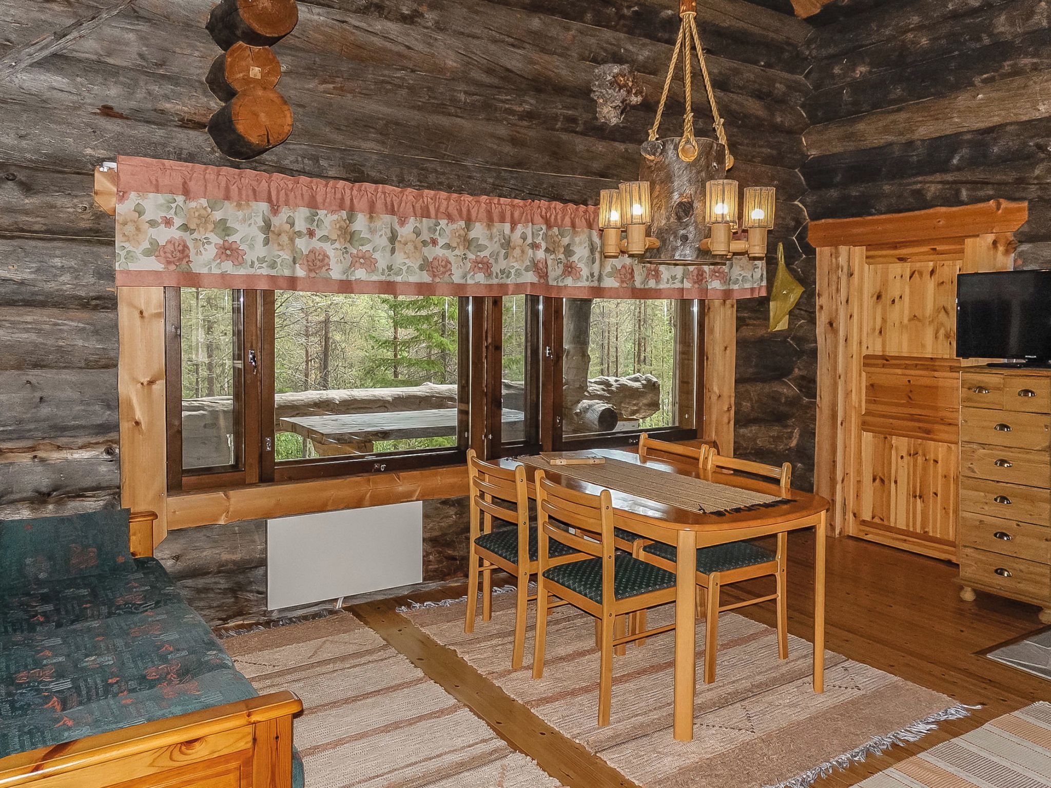 A rustic cabin interior with a dining table, chairs, a chandelier, and a television.