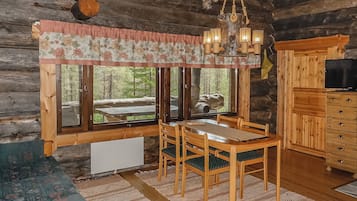 A rustic cabin interior with a dining table, chairs, a chandelier, and a television.