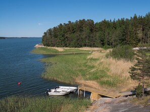 A calm lake with a dock and a boat, surrounded by dense forest and clear skies. - Merimetso by Interhome (Sauvo)