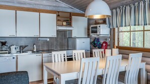 A modern kitchen with white cabinets, a dining table with chairs, a hanging light fixture, and a window with curtains. - Merimetso by Interhome (Sauvo)