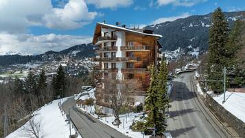 A multi-story building with balconies, a snow-covered landscape, and a mountainous backdrop.