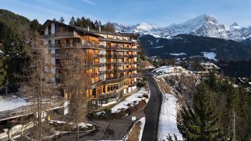 A multi-story hotel with balconies, a ski resort in the background, and a snow-covered landscape.