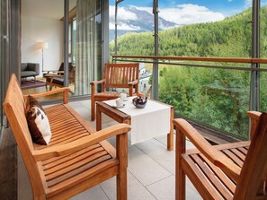 Un balcon agrémenté de meubles en bois, une table avec une théière, et une vue sur une chaîne de montagnes boisée.