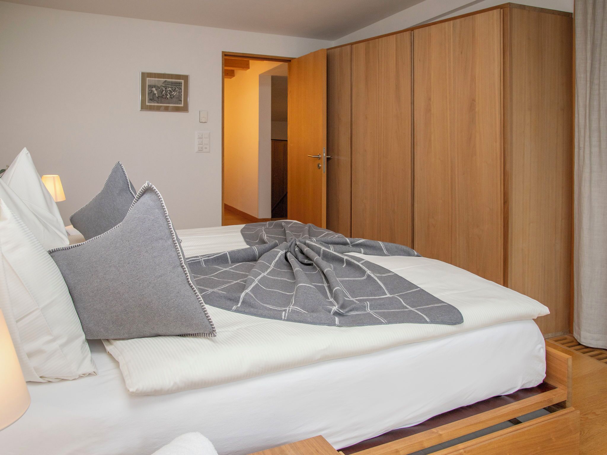Ein ordentlich bezogenes Bett mit grauer Decke und Kissen, ein Holzschrank und ein gerahmtes Bild an der Wand.