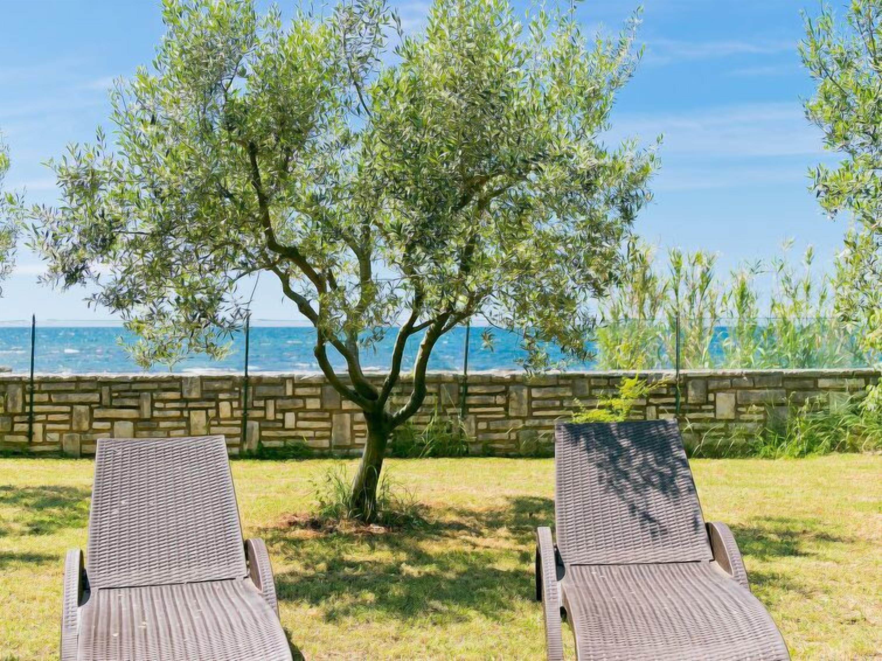 Due poltrone in vimini di fronte a un muro in pietra con vista sul mare.