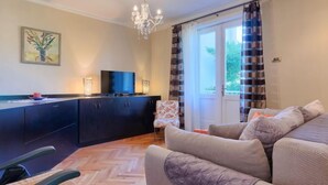 A living room with a sofa, a TV on a cabinet, a chandelier, and a window with curtains. - Vacation home Nona by Interhome (Umag)