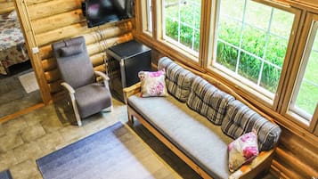 Ein Innenraum einer Blockhütte mit einer Couch, einem Sessel und einem an der Wand befestigten Fernseher.