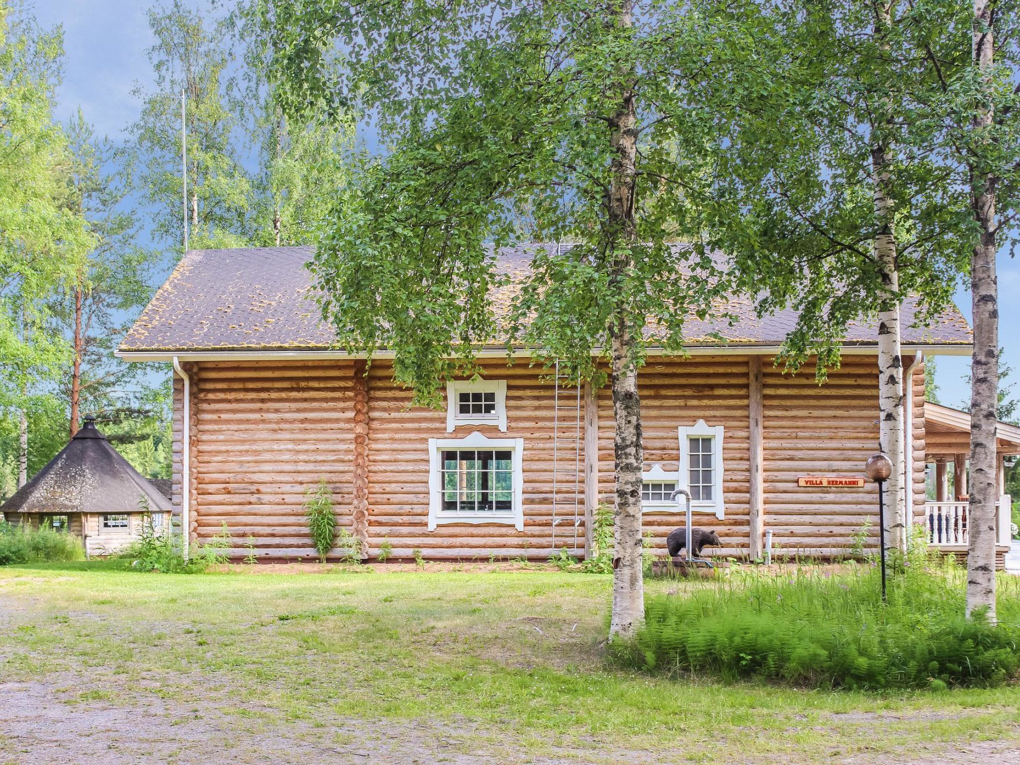 Hirsimökki, jossa on savupiippu, pieni kuisti ja kyltti, jossa lukee "Villa Hermann".