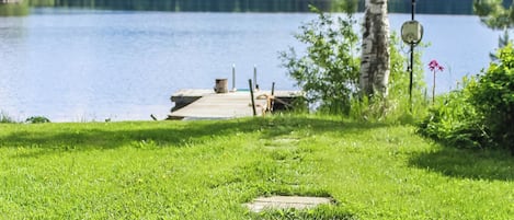 A grassy area with a wooden dock extending into a lake, surrounded by trees and a clear sky.