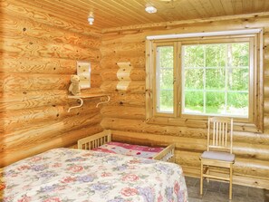 A wooden cabin room with a bed, a chair, a window, and a wall-mounted shelf. - Villa hermanni by Interhome (Pieksämäki)