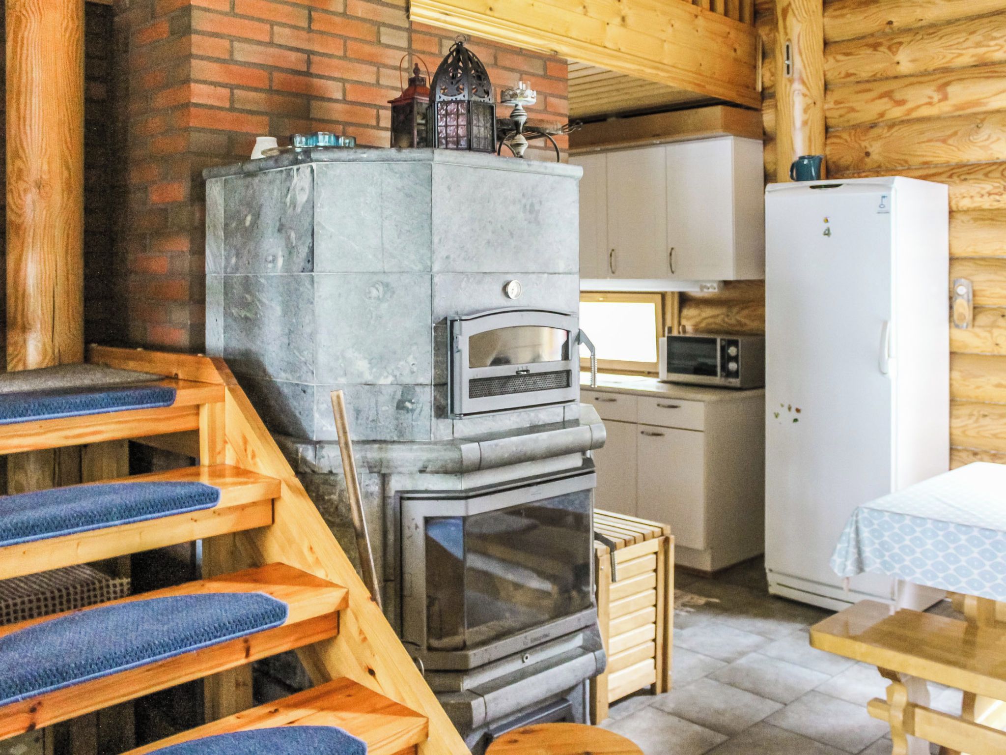 Een rustiek houten interieur met een stenen open haard, een houten trap, een keuken en een witte koelkast.