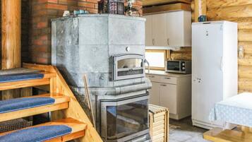 Een rustiek houten interieur met een stenen open haard, een houten trap, een keuken en een witte koelkast.