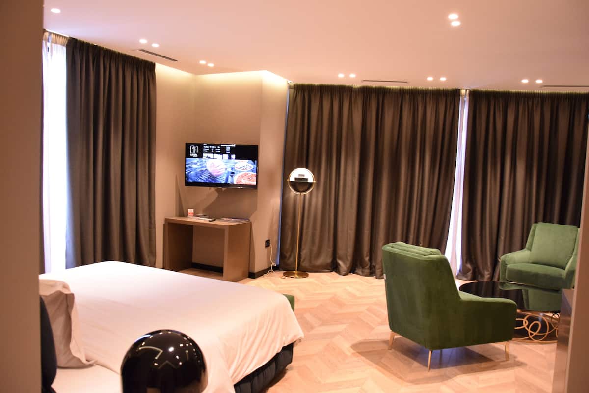 A hotel room with a bed, a television, a desk, and a green armchair.