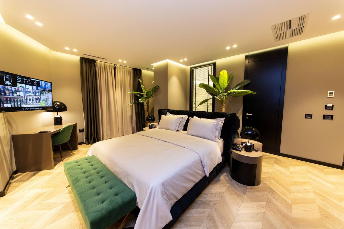 A modern hotel room with a large bed, a desk, and a TV displaying a room service menu.