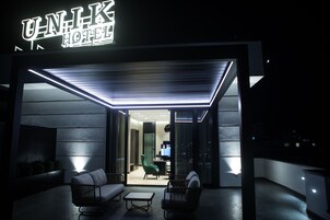 Exterior de un hotel de diseño moderno, con un letrero llamativo, una entrada bien iluminada y un área de descanso con sofá y sillones.