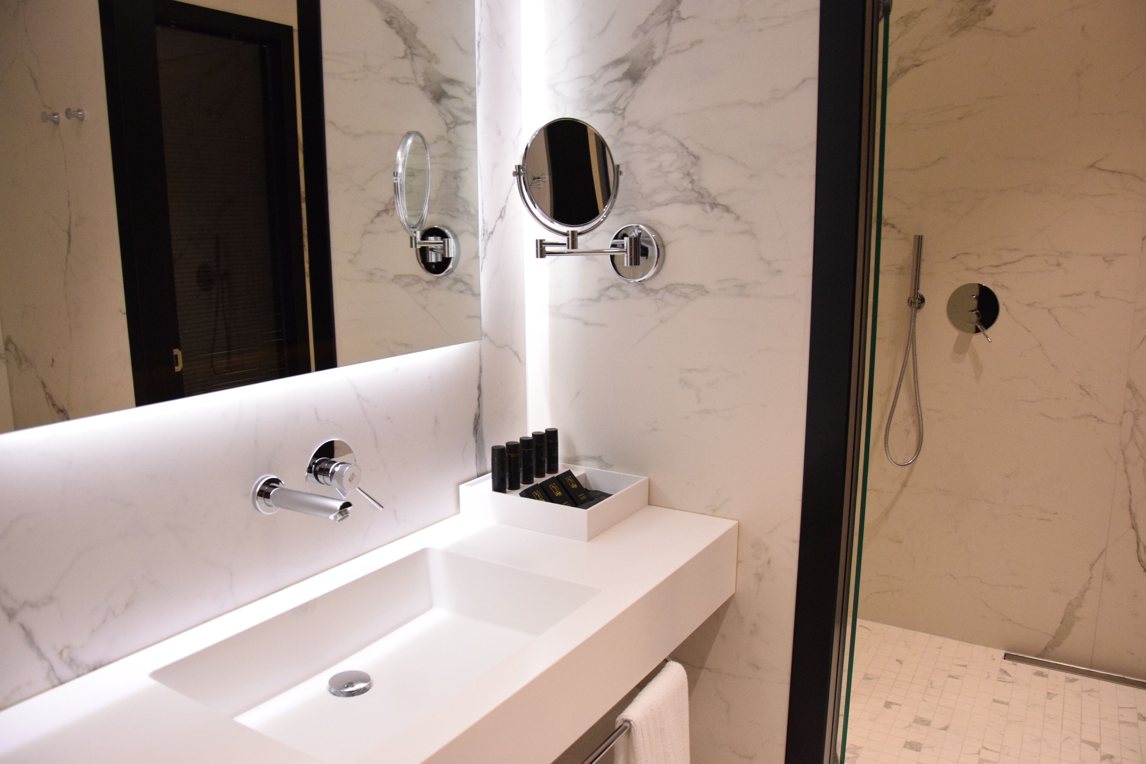 A modern bathroom with a large mirror, a white sink, and a shower area.
