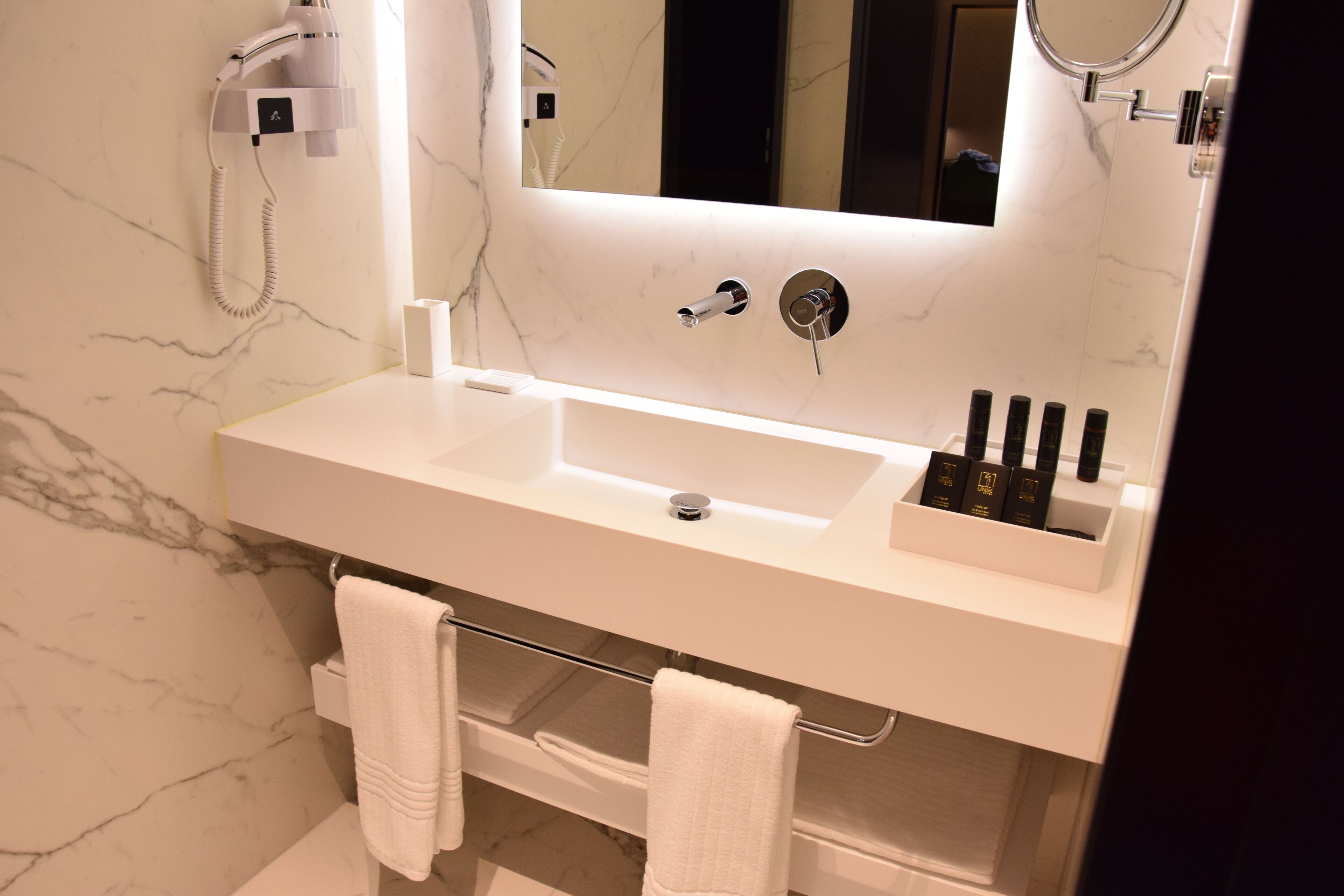 A modern bathroom with a white marble sink, a large mirror, and a towel rack.