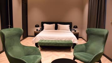 Una habitación de hotel con una cama, dos sillones verdes, una mesa redonda y una mesita de noche con lámpara.