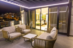 A balcony with wicker furniture, a glass door leading to a bedroom, and a cityscape view at night.