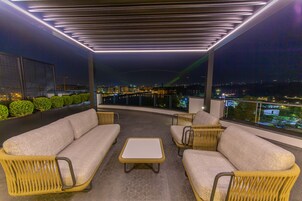 Un balcón con mobiliario de mimbre y vistas a la ciudad de noche.