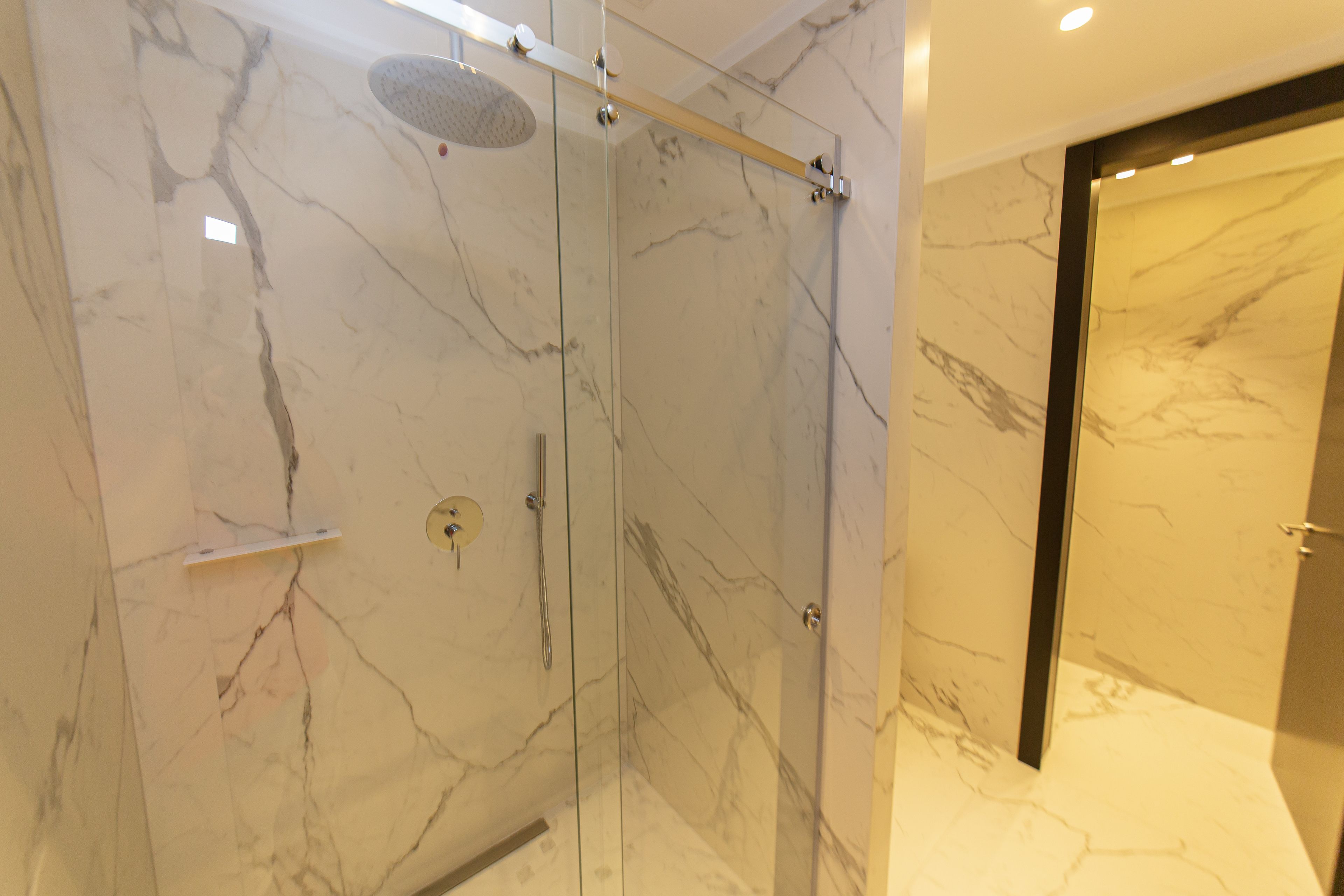 A modern bathroom with a glass-enclosed shower, marble walls, and a sleek door.