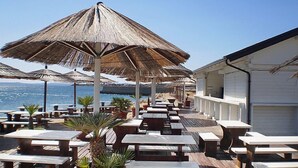Un restaurante frente al mar con mesas de madera y sombrillas de paja.