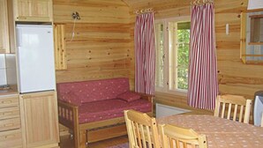 L’intérieur d’un chalet en bois comprend un coin cuisine, un canapé, une table à manger avec des chaises et des rideaux à rayures.