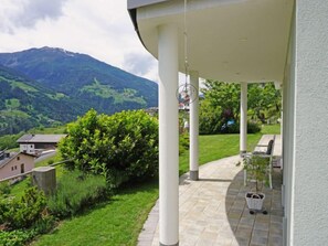 Un espacio al aire libre cubierto con vistas a una cordillera, un patio empedrado y un jardín con césped y arbustos.