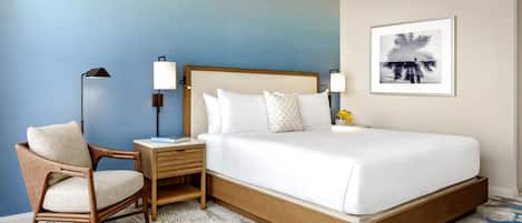 Quarto de hotel com uma cama grande, uma mesa de cabeceira, uma cadeira e uma luminária na parede.