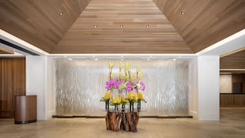 A modern lobby with a wooden ceiling, a round glass table with flowers, and a textured wall.