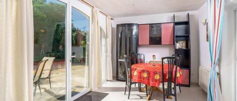 Ein sonnendurchfluteter Raum mit einer Schiebeglastür zu einer Terrasse, einem Deckenventilator, einem Esstisch mit Stühlen und einer eingebauten schwarzen Schrankwand.