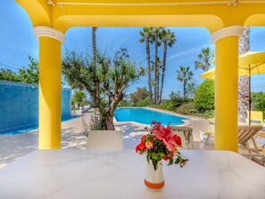 A poolside area with a marble table, yellow pillars, and a view of the pool and palm trees. - Villa Monte da Torre by Interhome (Loulé)