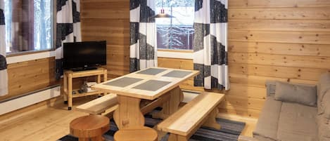 A cozy cabin interior with a wooden table, benches, a television, and a sofa.
