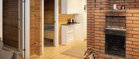 Een knus blokhutinterieur met houten vloer, een open haard, een keukenhoek en een zithoek.
