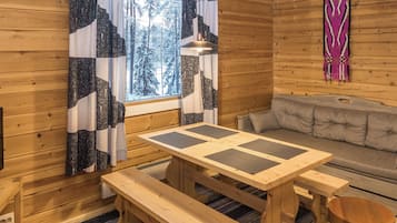 L’intérieur d’un chalet en bois, avec une table à manger, des bancs, un canapé et une fenêtre avec des rideaux.