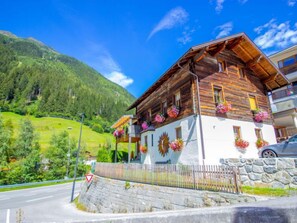 A wooden chalet with balconies adorned with flowers, set against a mountainous backdrop.