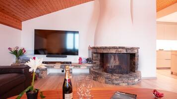 Ein modernes Wohnzimmer mit Kamin, Flachbildfernseher und einem Tisch mit einer Champagnerflasche und Gläsern.