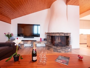 A modern living room with a fireplace, a flat-screen TV, and a table with a bottle of champagne and glasses. - Grand-Pont 15 by Interhome (Villars)